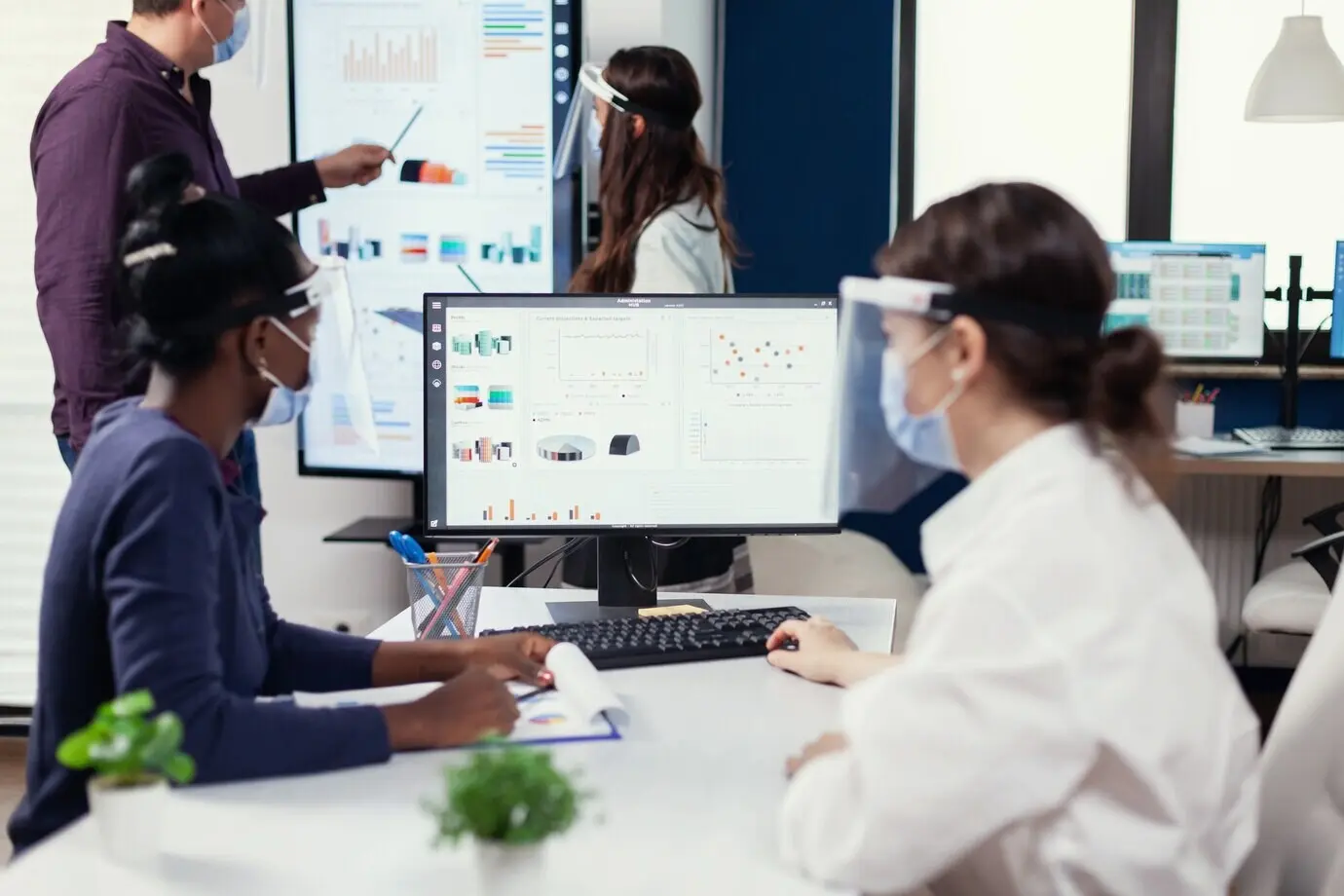 Сотрудник африканского происхождения слушает тренера на конференции по продажам во время COVID‑19. Многоэтническая команда работает в компании в условиях новой нормальности, соблюдая социальную дистанцию, во время глобальной пандемии коронавируса.